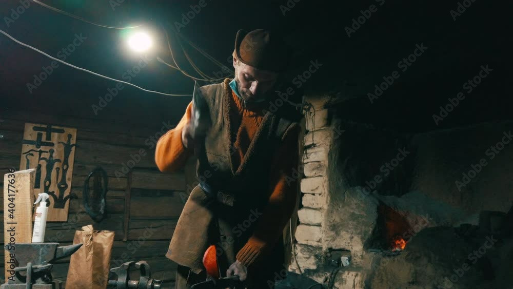 Young male blacksmith forges an ax in a smithy. Ancient hand craft culture. Preservation of historical values Young male blacksmith forges an ax in a smithy. Ancient hand craft culture. Preservation of historical values