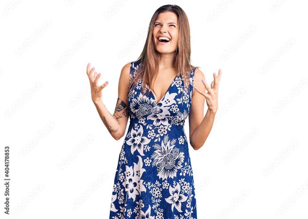 Beautiful caucasian woman wearing summer dress crazy and mad shouting and yelling with aggressive expression and arms raised. frustration concept. Beautiful caucasian woman wearing summer dress crazy and mad shouting and yelling with aggressive expression and arms raised. frustration concept.