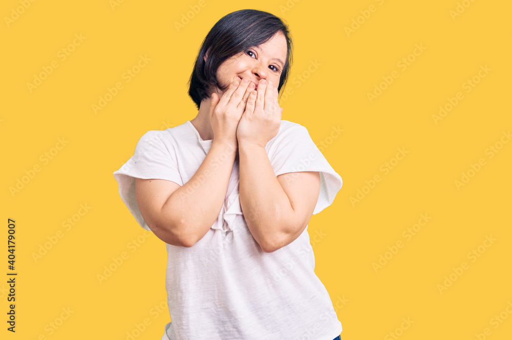 Brunette woman with down syndrome wearing casual white tshirt laughing and embarrassed giggle covering mouth with hands, gossip and scandal concept Brunette woman with down syndrome wearing casual white tshirt laughing and embarrassed giggle covering mouth with hands, gossip and scandal concept