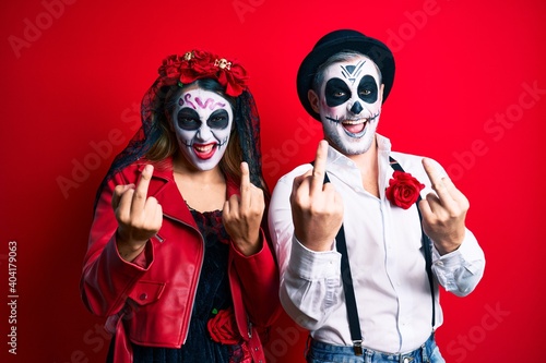Couple wearing day of the dead costume over red showing middle finger doing fuck you bad expression  provocation and rude attitude. screaming excited
