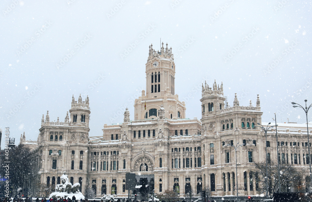 Madrid center of Cibeles square with the monument of the city hall in the background while snowing - cold winter postcard from Spain