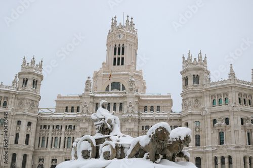 Madrid cityscape in winter with the Cibeles monument and the city hall palace covered in snow - cold empty postcard from Spain