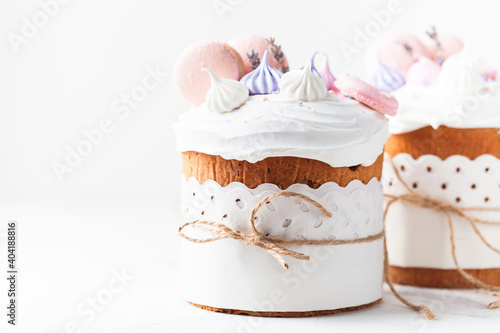 Easter cake  sweet bread decorated with white sugar icing  meringues and macaroons. Kulich wrapped in a craft paper on the white background.