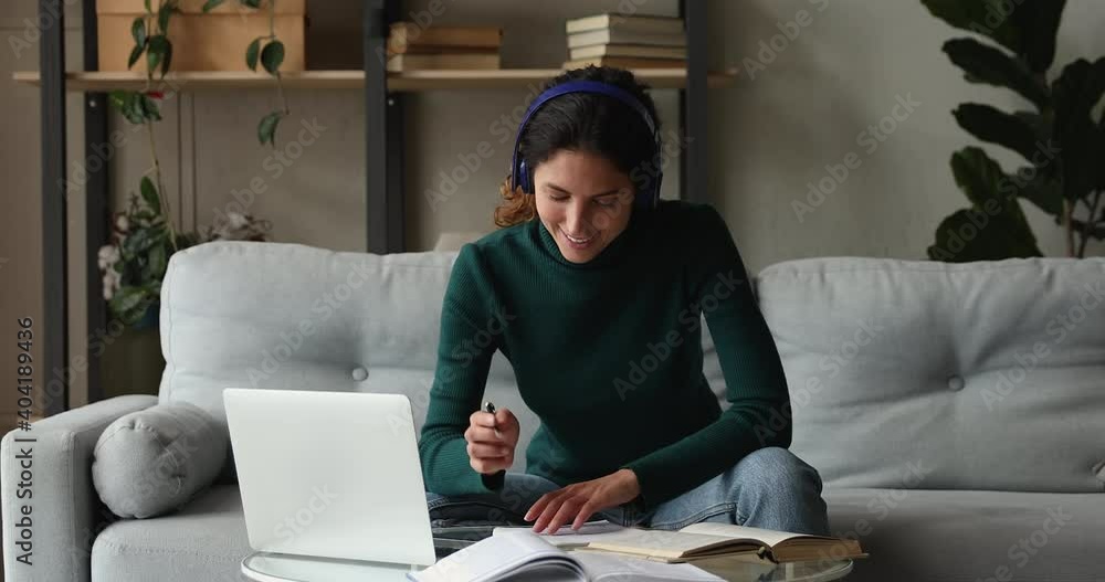 Millennial woman sit on couch wear headphones talk by videoconference app on laptop writes notes learn foreign language with online tutor at home. Remote work use modern tech, video call event concept Millennial woman sit on couch wear headphones talk by videoconference app on laptop writes notes learn foreign language with online tutor at home. Remote work use modern tech, video call event concept