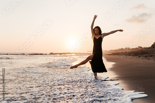 Freedom Chinese woman feeling free dancing in black elegant dress at beach sunset. Healthy living Asian girl on summer travel vacation. Success, happiness, mindfulness concept.