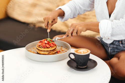 Fototapeta Naklejka Na Ścianę i Meble -  Beautiful young woman eating pancakes in a cafe for breakfast