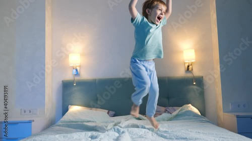 Happy laughing and smiling toddler boy in pajamas skipping and jumping up high on parent's bed at night before going to sleep photo