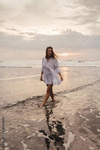 young woman wearing beautiful white dress is walking on the beach during sunset. Bali Indonesia