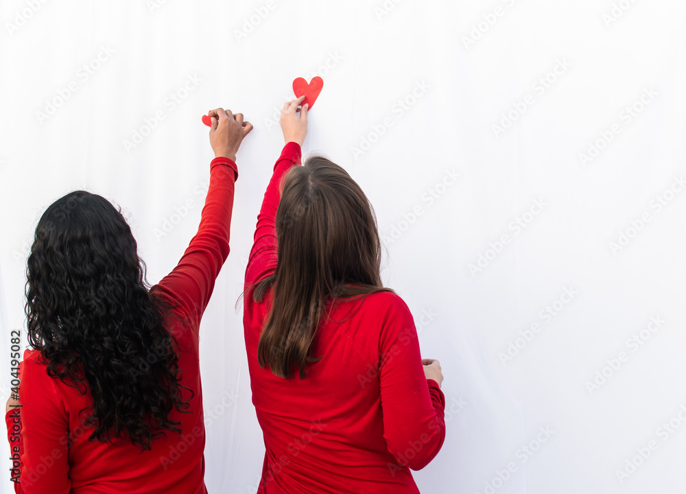BLONDE WOMAN WITH BRUNETTE WOMAN STICKING HEARTS AND CELEBRATING BLONDE WOMAN WITH BRUNETTE WOMAN STICKING HEARTS AND CELEBRATING