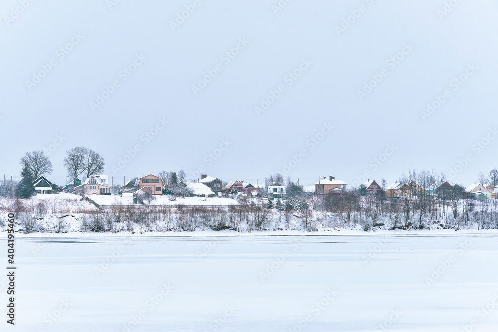 View of the village by the river. Rural landscape. Yaroslavl region, Russia. Motion blur of snowfall.
