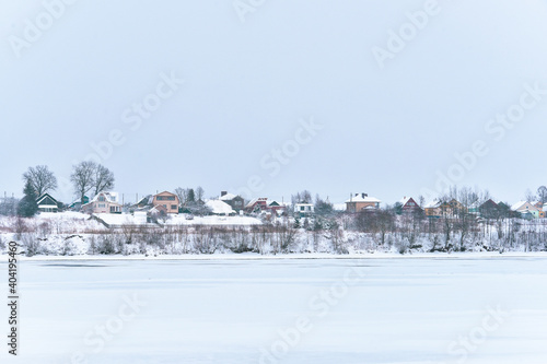 View of the village by the river. Rural landscape. Yaroslavl region, Russia. Motion blur of snowfall.