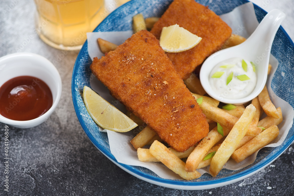 Deep-fried breaded fish fillet with french fries and dips served in a blue bowl, closeup, studio shot Deep-fried breaded fish fillet with french fries and dips served in a blue bowl, closeup, studio shot