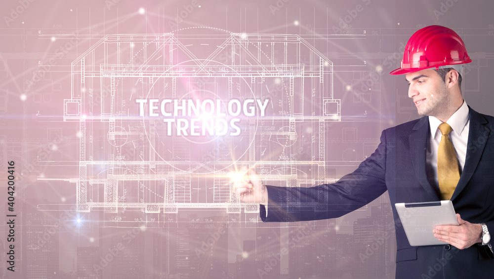 Handsome architect with helmet drawing TECHNOLOGY TRENDS inscription, new technology concept Handsome architect with helmet drawing TECHNOLOGY TRENDS inscription, new technology concept