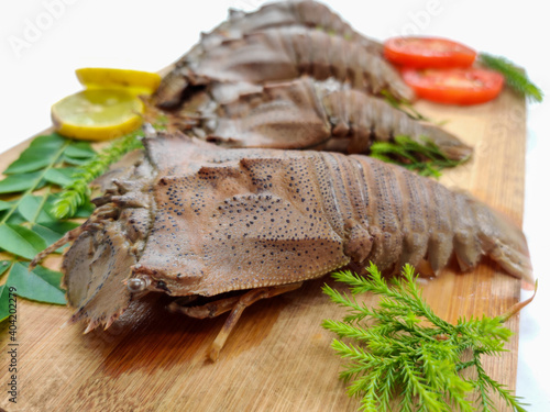 Fresh Sand Lobster or Flathead Lobster or Slipper Lobster (Thenus Orientalis) decorated with herbs and vegetables on a wooden pad.White Background,Selective Focus. photo