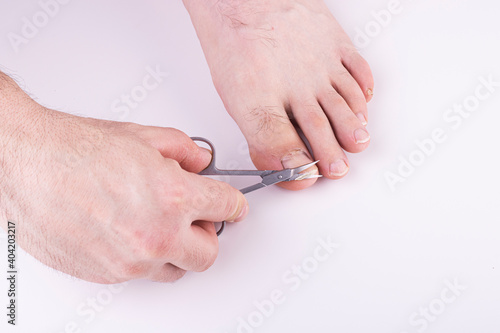 men s hands cut their toenails with scissors on a white background