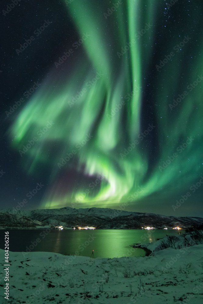 Huge northern lights (aurora borealis) over a beach and fjord in arctic Norway