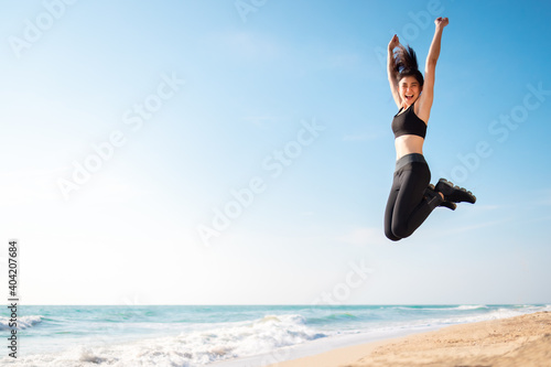 Young Asian healthy athletic slim woman smiling jumping on beach