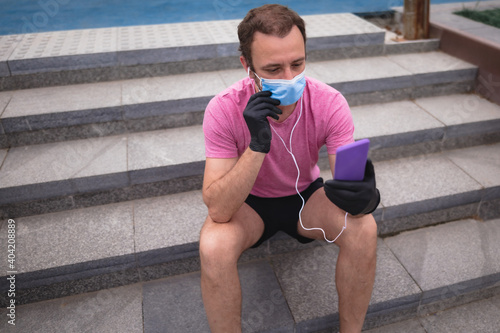 Sportsman with medical mask and gloves, smartphone and earbuds working out, jogging in urban surroundings.