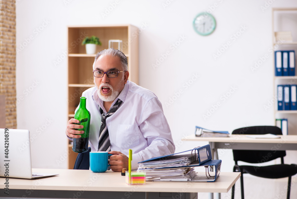 Old male employee drinking alcohol in the office