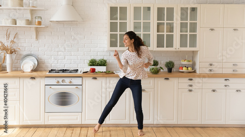 Happy young Caucasian woman renter enjoy good morning in new cozy renovated modern kitchen. Smiling millennial female tenant have fun dancing at home, celebrate relocation or moving to own house.