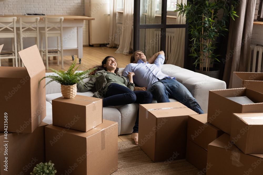 Overjoyed millennial couple renters lying relaxing on sofa tired after relocating to new home. Happy young Caucasian man and woman rest on couch in living room on moving day to own house. Overjoyed millennial couple renters lying relaxing on sofa tired after relocating to new home. Happy young Caucasian man and woman rest on couch in living room on moving day to own house.
