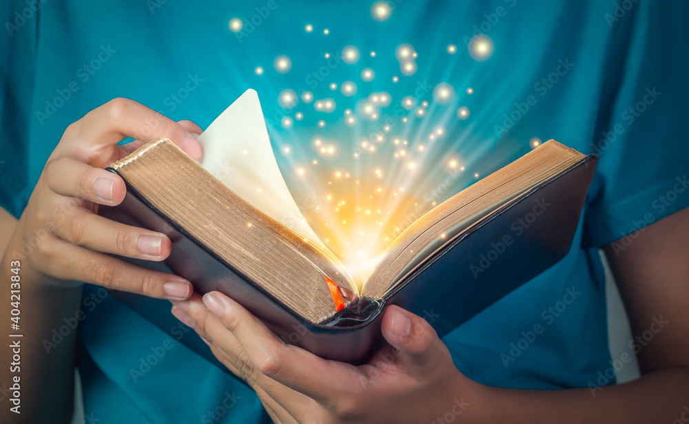 Hand of child opening the gold edge magic book with mystic bright spark light on dark background. Fantasy and discovery magic concept.