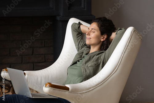 Happy calm young Caucasian woman sit relax in comfortable armchair distracted from computer work sleep or np. Relaxed female rest in chair relive negative emotions. Stress free, peace concept. photo