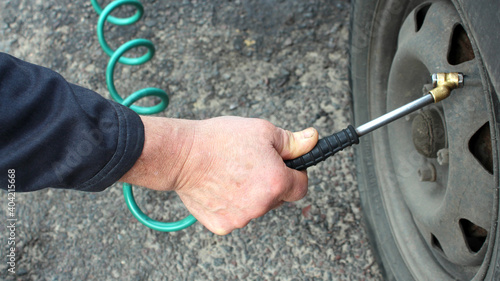 In a man's hand there is a hose from a compressor pumping up a car wheel. Close-up.