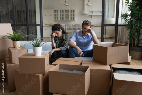 Tired unhappy young Caucasian couple sit on sofa in new living room feel unmotivated unpacking. Upset stressed millennial man and woman have fight quarrel unboxing packages relocating moving. © fizkes