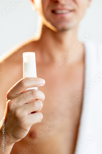 Male skincare. Cosmetic product. Body moisturizing. Cropped portrait of satisfied shirtless man showing small white mockup tube with lotion or cream smiling isolated on blur light background.