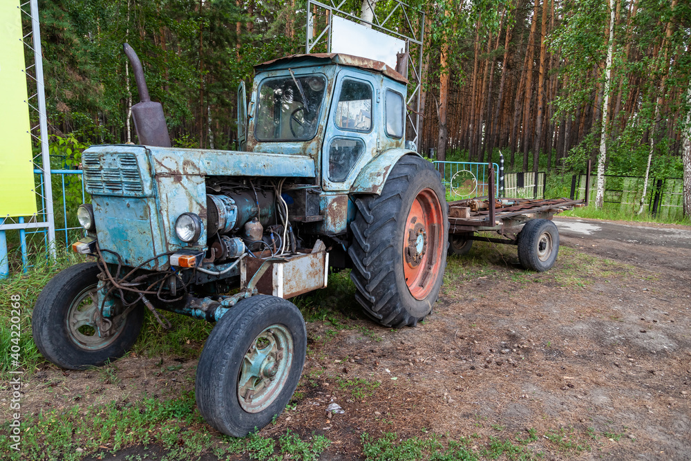 Old rusty Belarusian tractor stot at the entrance to the village of Ordynskoye as a monument to agriculture. Scrap metal recycling.