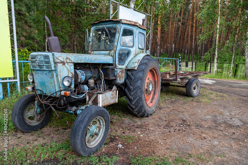 Old rusty Belarusian tractor stot at the entrance to the village of Ordynskoye as a monument to agriculture. Scrap metal recycling.