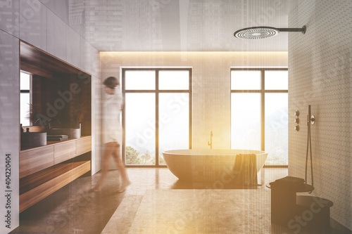 Woman walking in white and wooden bathroom with tub and shower