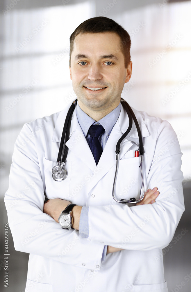 Professional doctor with a stethoscope is standing straight with crossed arms in a sunny clinic. Perfect medical service in a hospital. Best healthcare concept Professional doctor with a stethoscope is standing straight with crossed arms in a sunny clinic. Perfect medical service in a hospital. Best healthcare concept