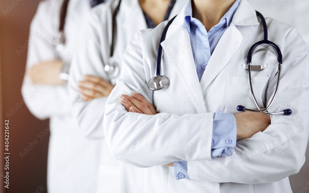 Group of modern doctors standing as a team with arms crossed in sunny hospital and ready to help patients. Medical help, insurance in health care Group of modern doctors standing as a team with arms crossed in sunny hospital and ready to help patients. Medical help, insurance in health care