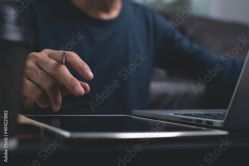 Casual man working on laptop computer and using digital tablet at home , close up, work from home concept