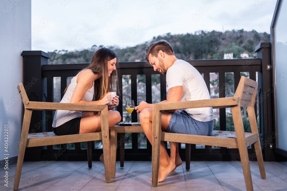 A Caucasian couple having breakfast on the hotel terrace in pajamas. Toasting with orange juice in the morning, lifestyle of a couple in love