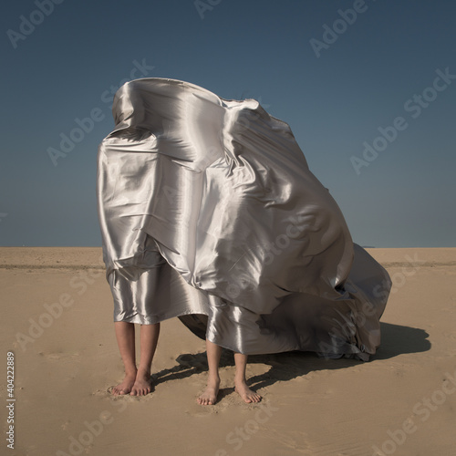 Two children covered by silver shiny drapes standing on the beach on a windy day photo