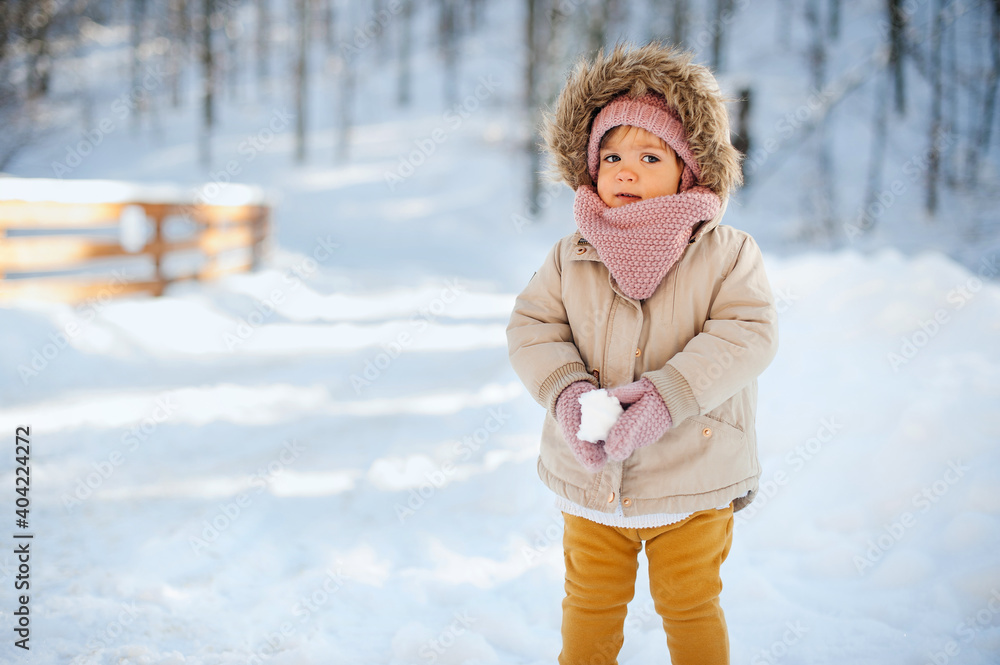 Adorable baby girl in a warm snow suit playing in snow on a very sunny and clear winter day in a park.