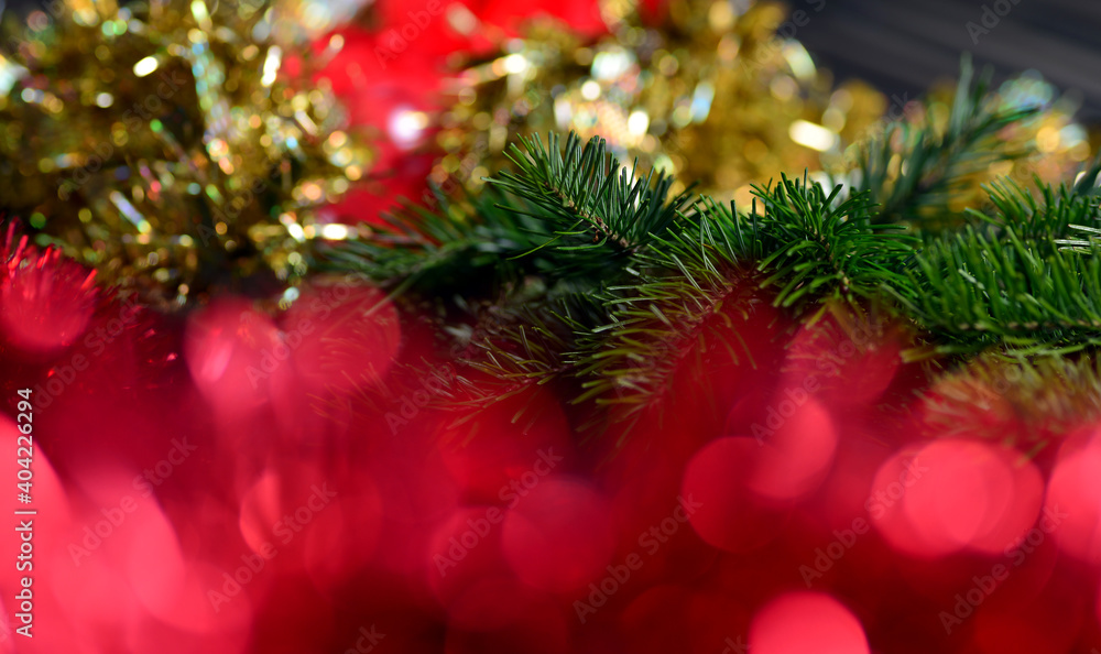 Christmas background with gold tinsel and red blurred lights, green spruce branches.