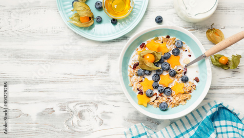 Healthy breakfast. Fresh granola, muesli with milk, honey and berries. White wooden background. Top view