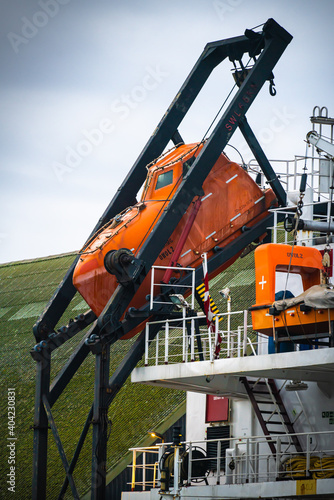 Industrial grade orange quick life boat mounted on the stern a cargo ship at port.