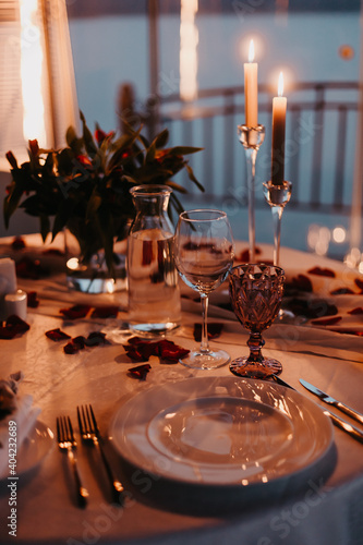 Luxury romantic candlelight dinner for couple. Table setup with candles and rose petals at night. Valentine decoration