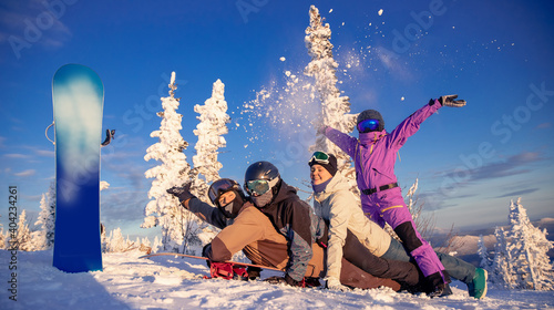 Happy group snowboarders friends woman and man at Sheregesh winter ski resort, In background trees and mountains in snow with sunset