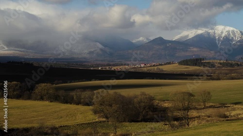 Timelapse of clouds over High Tatras rocky mountains and Strane pod Tatrami village in windy winter day, Slovakia. Landscape of fields and meadows under mountains not covered with snow due to climate 