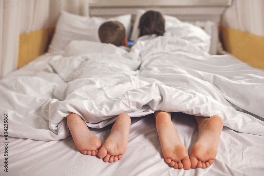 Two siblings watching video in their mobile electronic device in the bed, gadget dependence and addiction, online and internet for the whole day, family lifestyle, indoor Two siblings watching video in their mobile electronic device in the bed, gadget dependence and addiction, online and internet for the whole day, family lifestyle, indoor