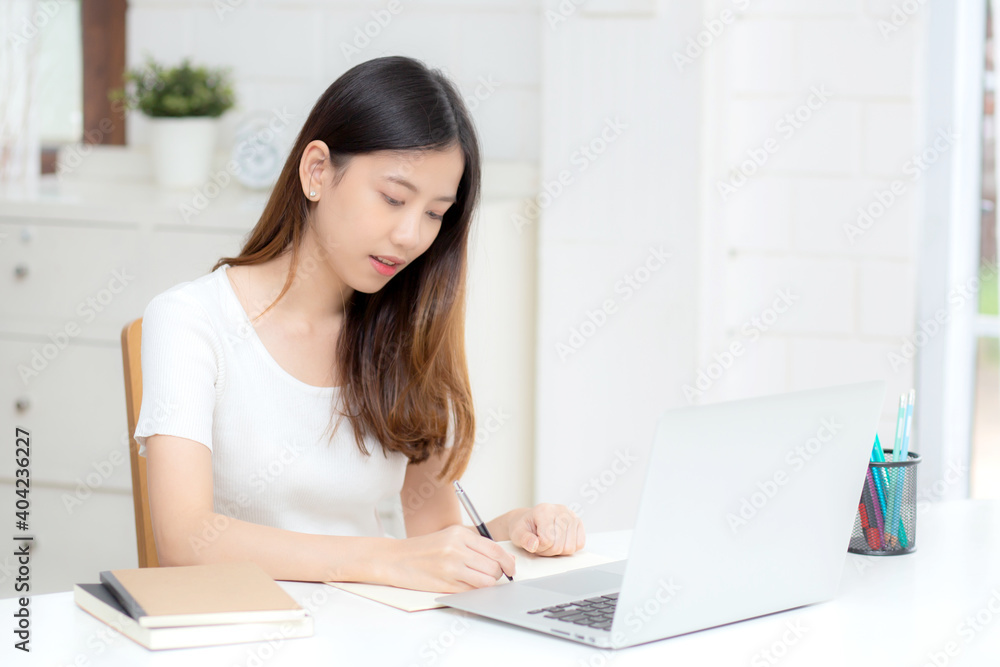 Young asian woman writing on notebook for planning working and using laptop computer on desk at home, girl notes about finance, female study and learning, business and communication concept. Young asian woman writing on notebook for planning working and using laptop computer on desk at home, girl notes about finance, female study and learning, business and communication concept.