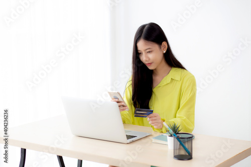 Young asian business woman using smart phone and holding credit card while online shopping and payment online with laptop computer on desk at home, female holding debit card, communication concept. © N_studio