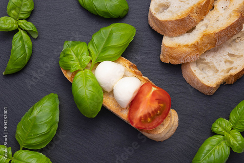 on a black stone stand are crackers with a small mozzarella, basil and chopped tomatoes and other croutons photo