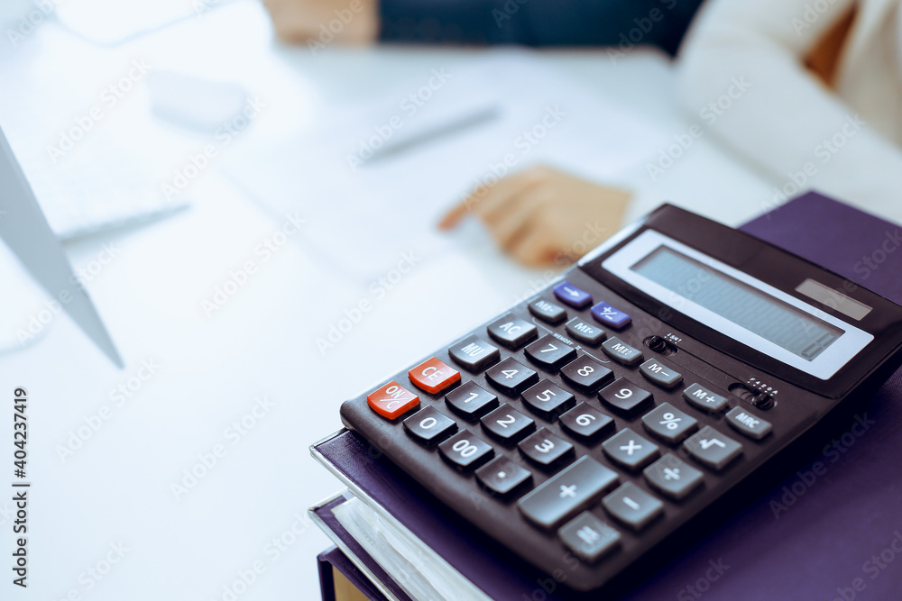 Calculator and binders with papers are waiting to be processed by business woman or bookkeeper working at the desk in office back in blur. Internal Audit and tax concept Calculator and binders with papers are waiting to be processed by business woman or bookkeeper working at the desk in office back in blur. Internal Audit and tax concept